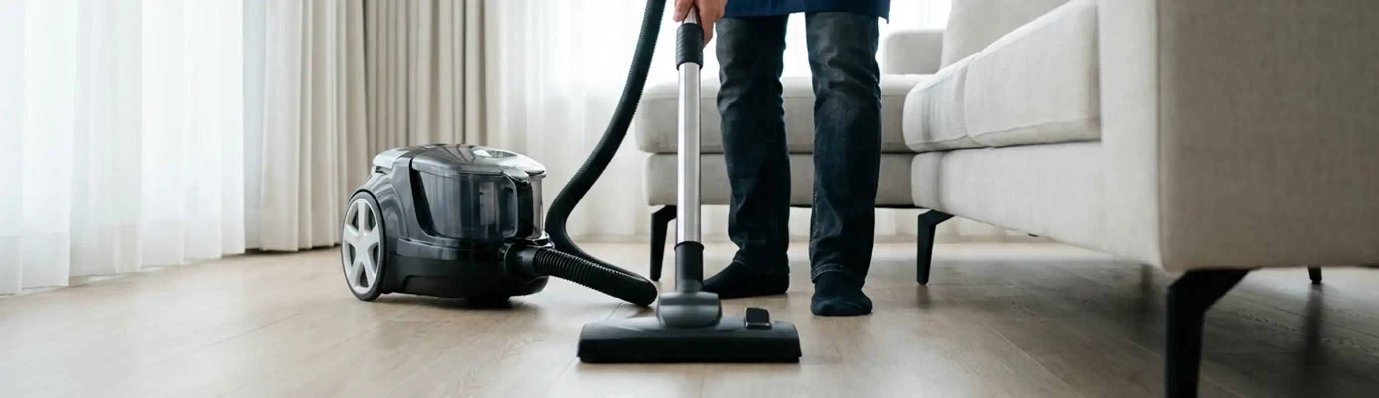 Professional house cleaner vacuuming a living room floor with a canister vacuum cleaner, Marietta, GA.
