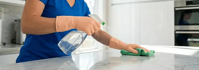 Maid service worker spraying and wiping a kitchen countertop with a microfiber cloth for sanitizing, Marietta, GA.