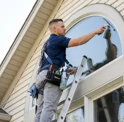 Professional window cleaner on a ladder using a squeegee to clean an exterior arched window, Marietta, GA.