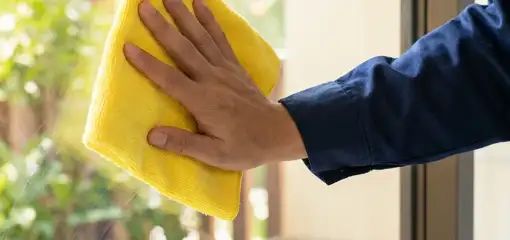 House cleaner wiping a glass window with a yellow microfiber cloth for streak-free cleaning, Marietta, GA.